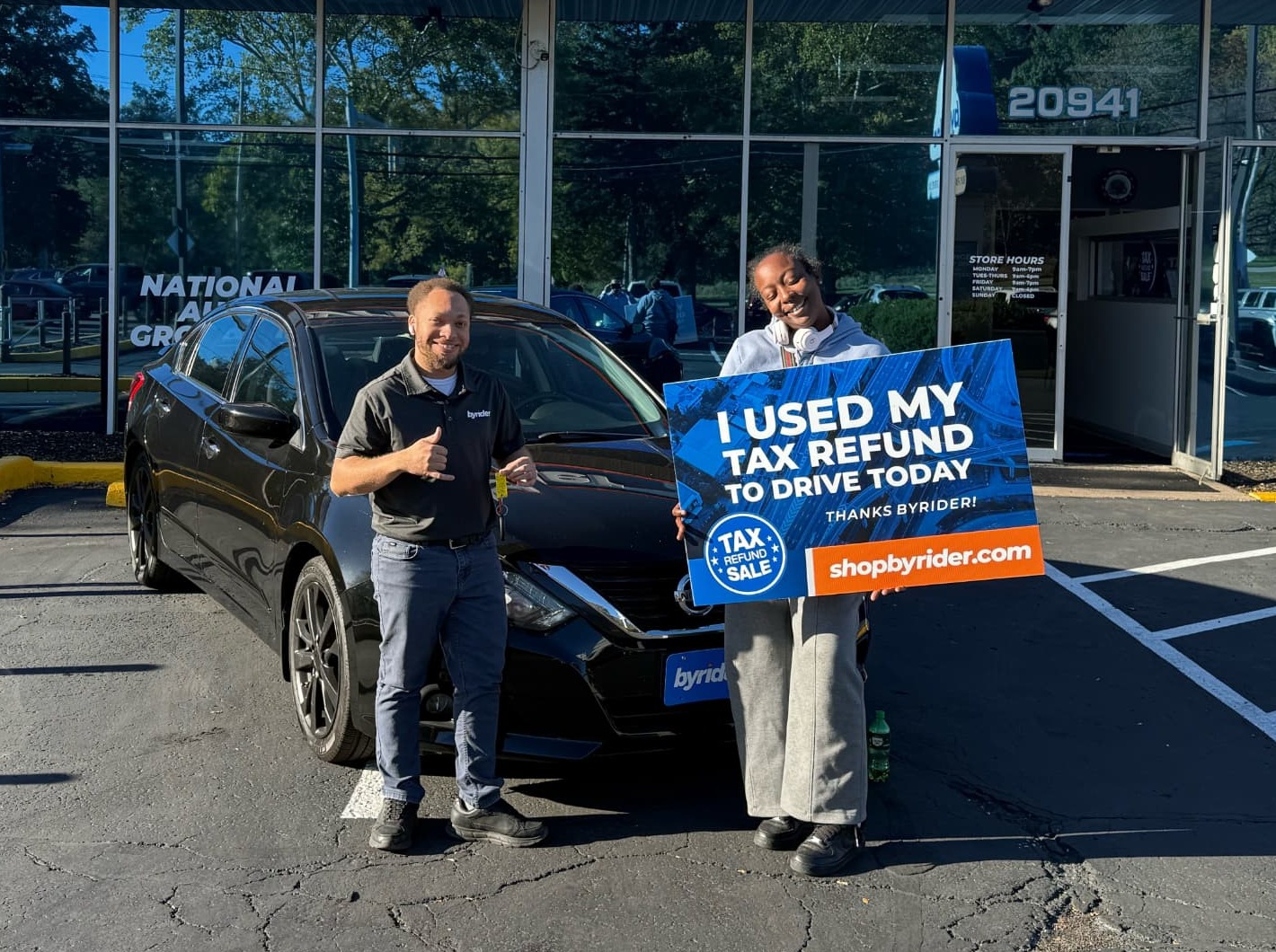 Byrider team member celebrating with a customer holding an I Used My Tax Refund to Drive Today sign next to her Nissan Sentra in Ohio