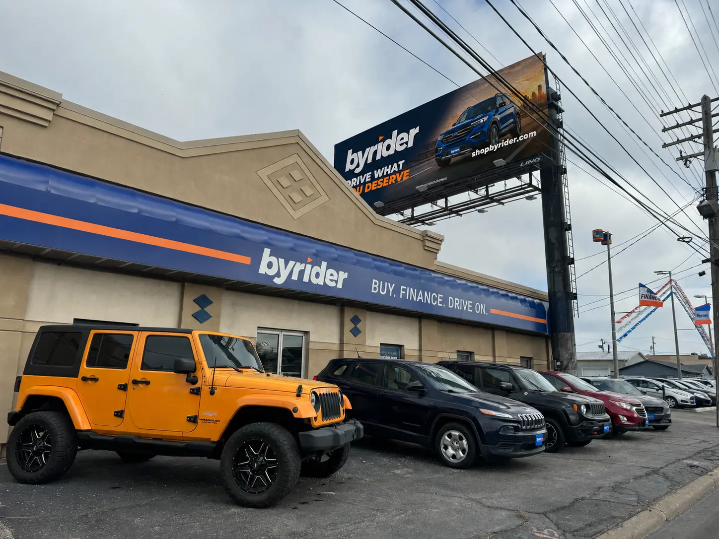 Byrider Cleveland used car dealership storefront at 5250 Brookpark Rd, Parma, Ohio, with a yellow Jeep Wrangler and rows of SUVs on the lot